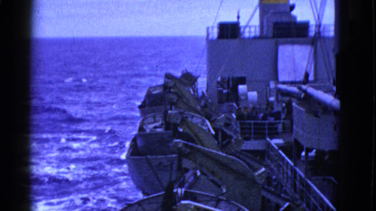 Ship deck and lifeboat equipment seen over open ocean with heavy blue film cast.