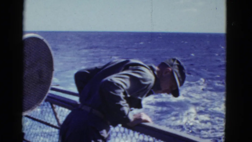 In supported 1950s San Francisco-area footage, a uniformed man bends over a ship railing while looking toward the sea.