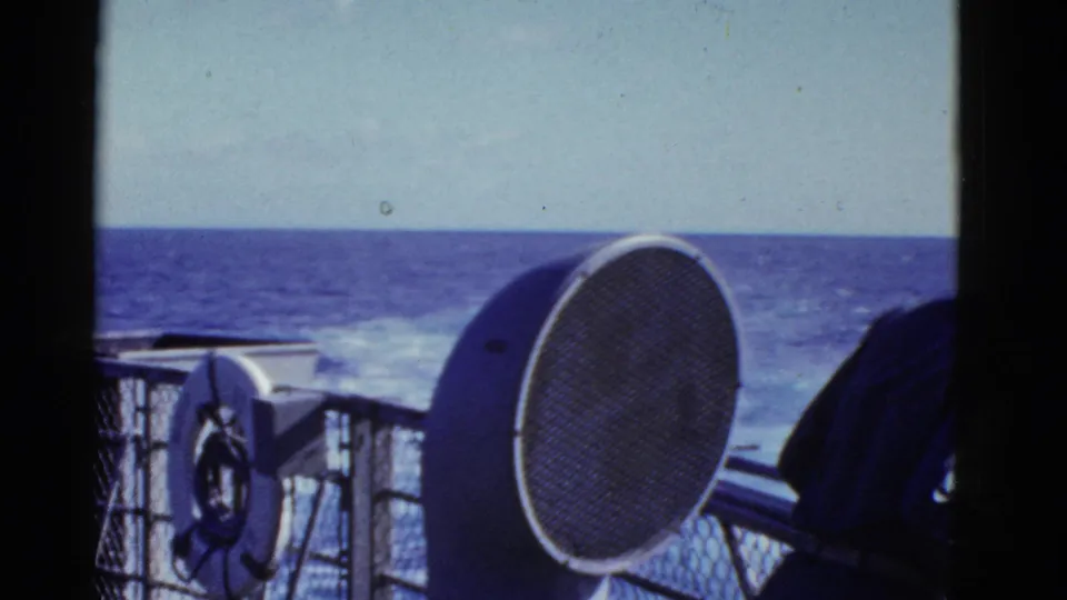 The frame centers deck fixtures, a life preserver and ocean horizon while the uniformed figure is mostly cropped at right.