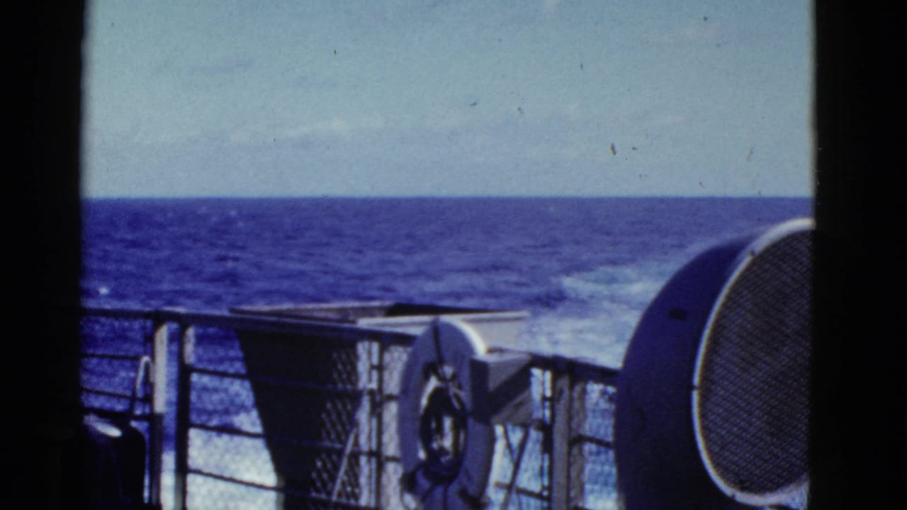 Ship railing and deck equipment facing open ocean under a pale sky.