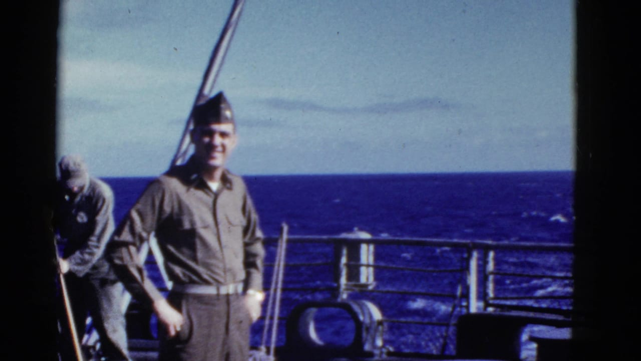 Uniformed man smiling on a ship deck with ocean behind him.