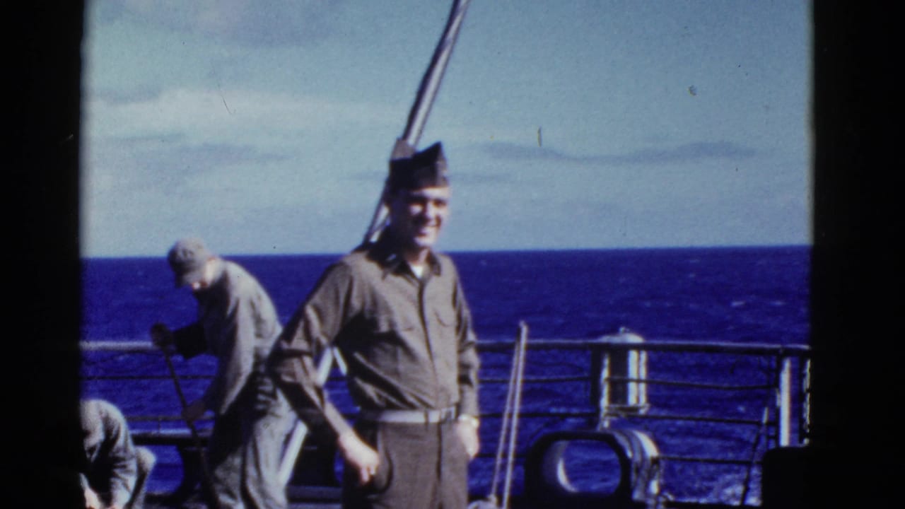 Early-1950s shipboard frame showing a uniformed man near the camera and another man handling equipment by the ocean rail.
