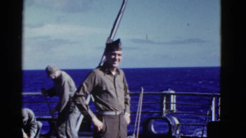 Early-1950s shipboard frame showing a uniformed man near the camera and another man handling equipment by the ocean rail.