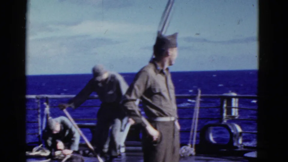Early-1950s 8mm frame of a uniformed man turning on deck as other men handle ropes or gear near the rail at sea.