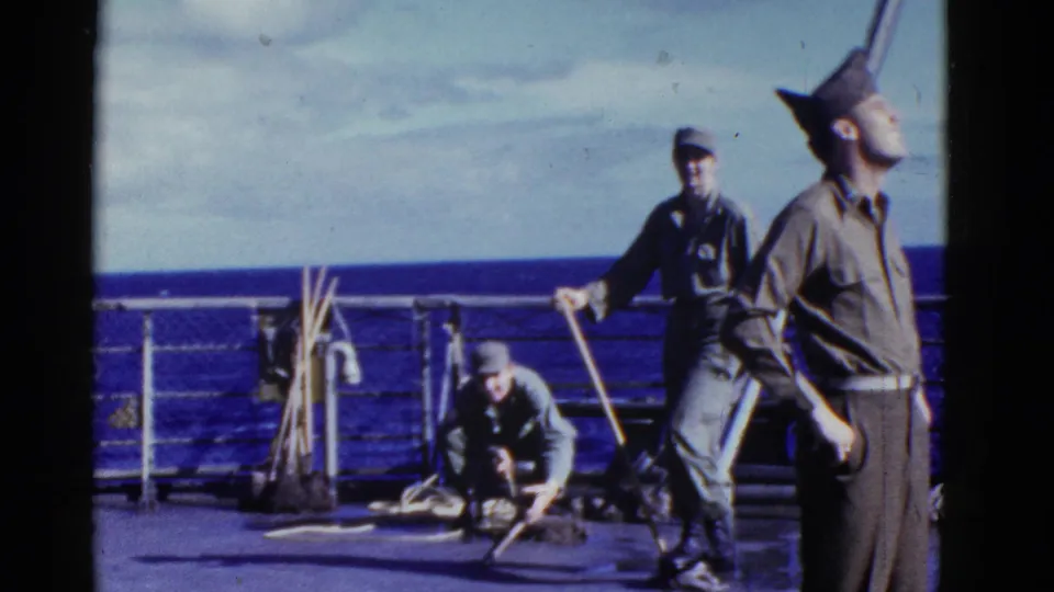 Early-1950s shipboard frame with multiple uniformed men, deck gear, railings, and open ocean visible behind them.