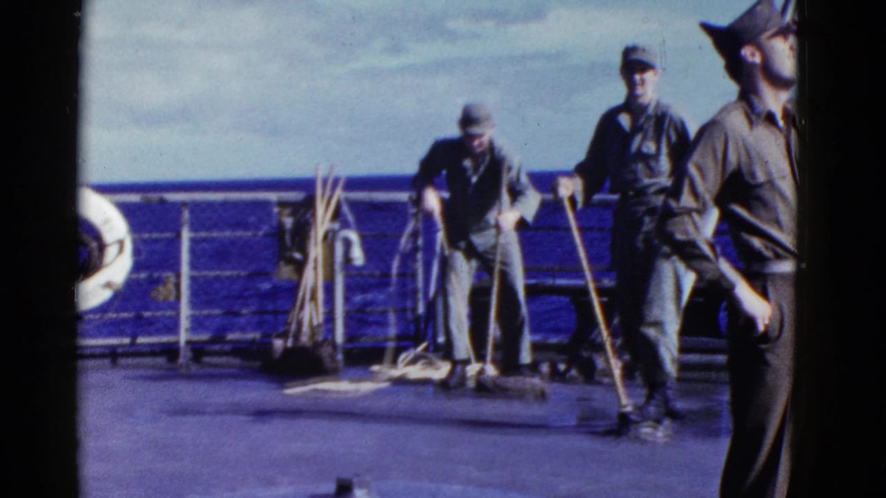 1950s 8mm frame of men on a navy vessel deck, with workers sweeping near ropes, railings, and open ocean.