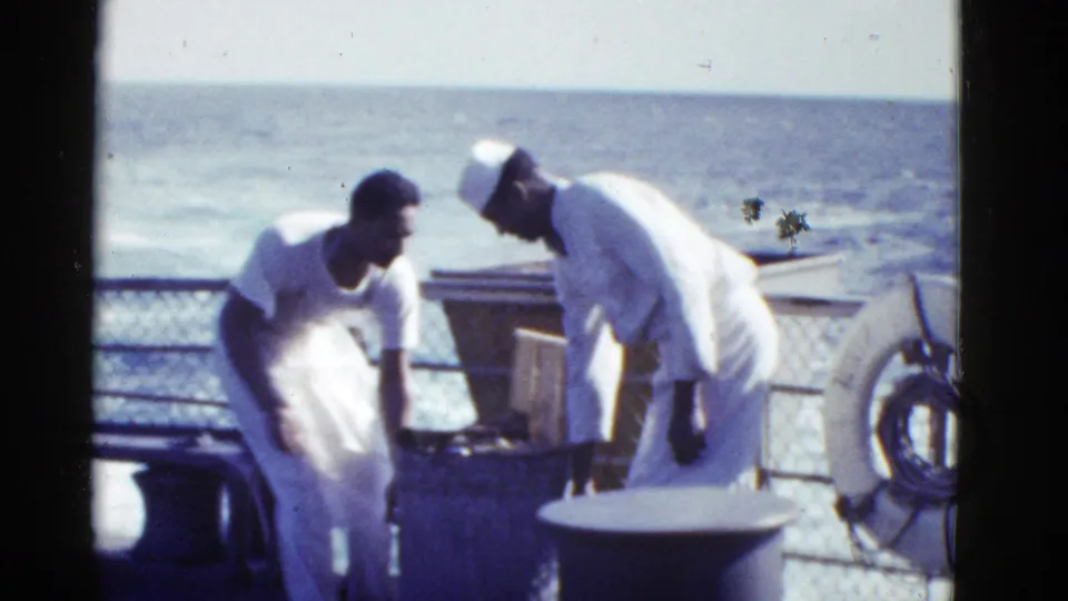 Two sailors in white naval attire appear to confer beside ship deck fittings, railings, ocean, and a visible life ring.