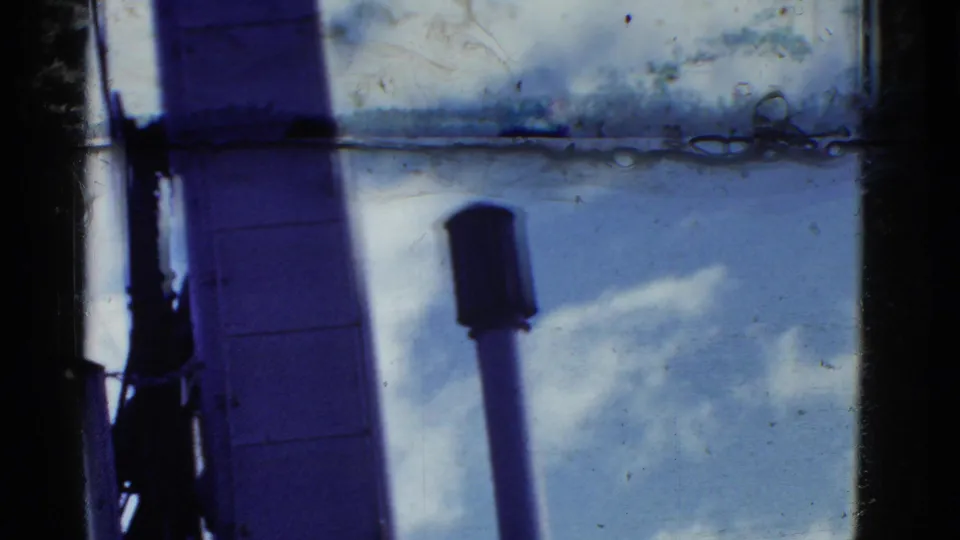 A brief 8mm frame shows ship structure and a vertical deck pipe or vent, with sky and soft film marks visible.