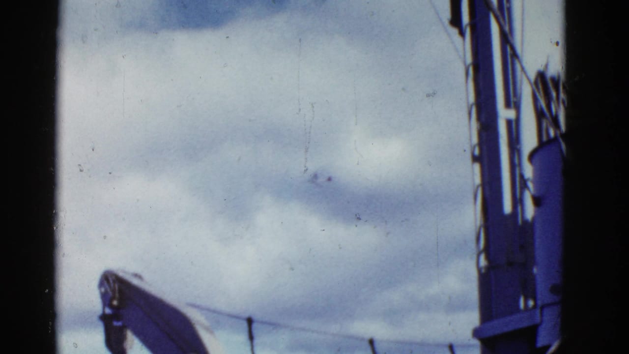 1950s 8mm home-movie frame near San Francisco showing cloudy sky, shipboard rigging, and a blue mast or boom along the edge.