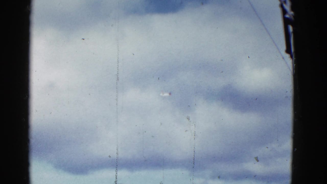 Cloud-filled sky divided by dark vertical film edges, with dust and scratch marks visible.