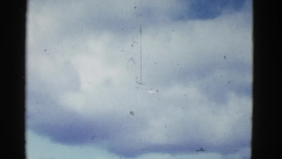 Soft 8mm view of clouds over a pale blue sky, with film scratches and dust marking the home-movie scan.