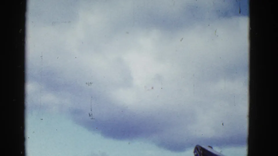 Final 1950s 8mm frame showing cloudy sky with a small rigging or structure detail at lower right and visible film wear.
