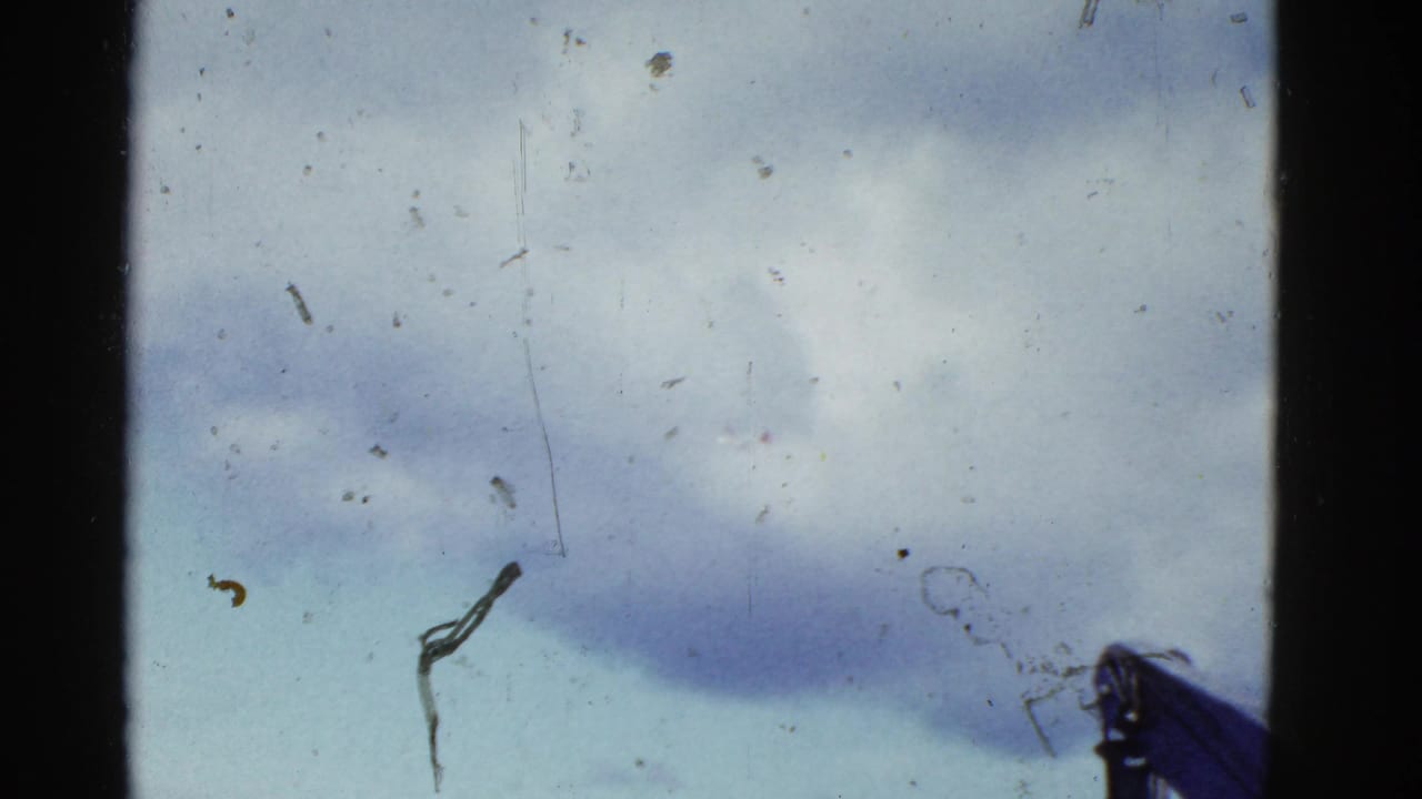Cloudy blue sky with film borders, dust, and a partial hat at the bottom edge.
