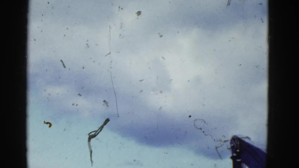 1950s 8mm home-movie frame looking up at a cloudy San Francisco sky with film wear and a partial hat visible below.