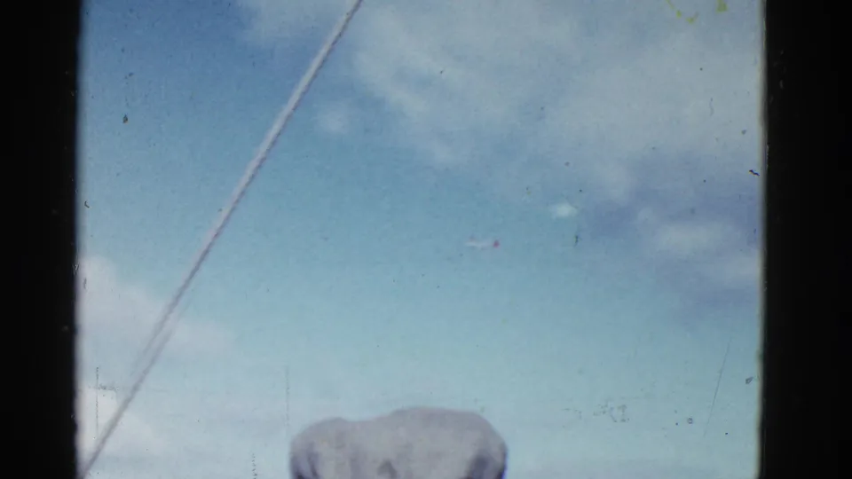 Faded 8mm view of cloudy San Francisco sky with a partial cap below and a prominent diagonal film scratch.
