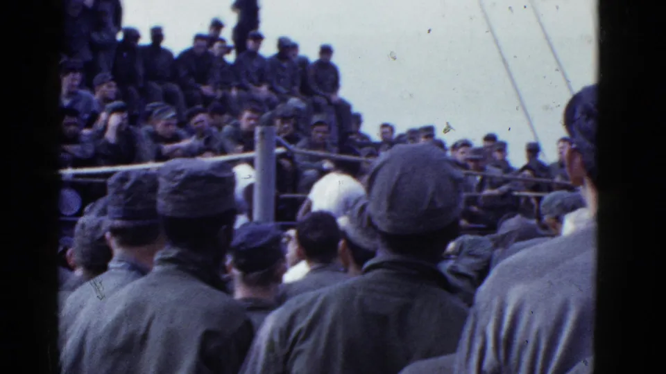 1950s 8mm frame of uniformed servicemen gathered around a roped boxing area on a vessel near San Francisco.