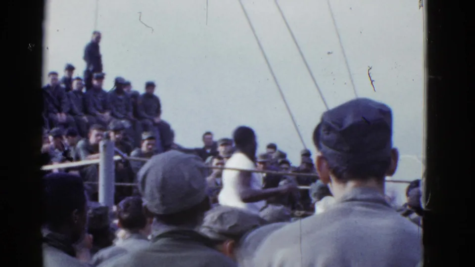 The frame shows a boxer near the roped area with uniformed spectators gathered across the ship deck in 1950s home-movie footage.