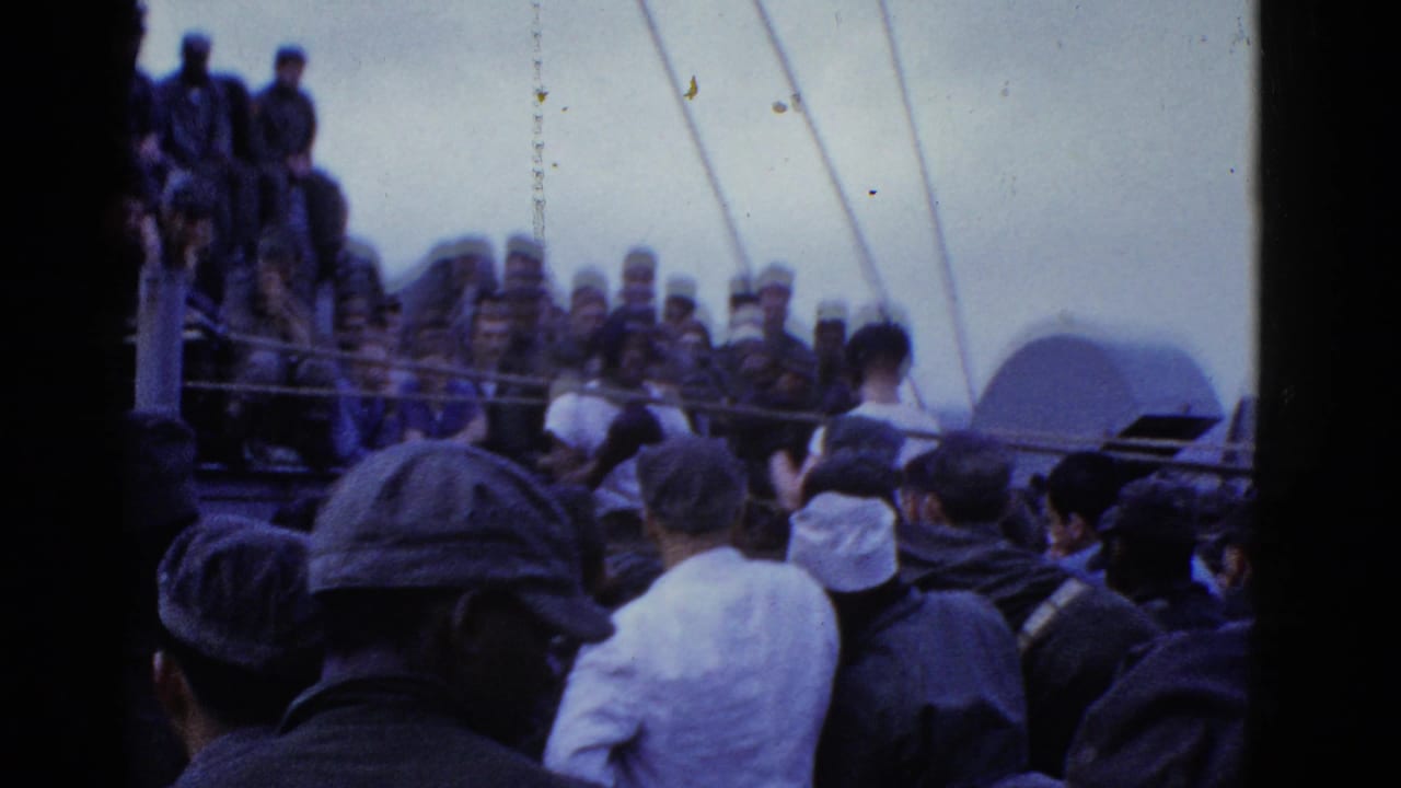 Crowded ship deck with men in caps facing a seated group near railings.