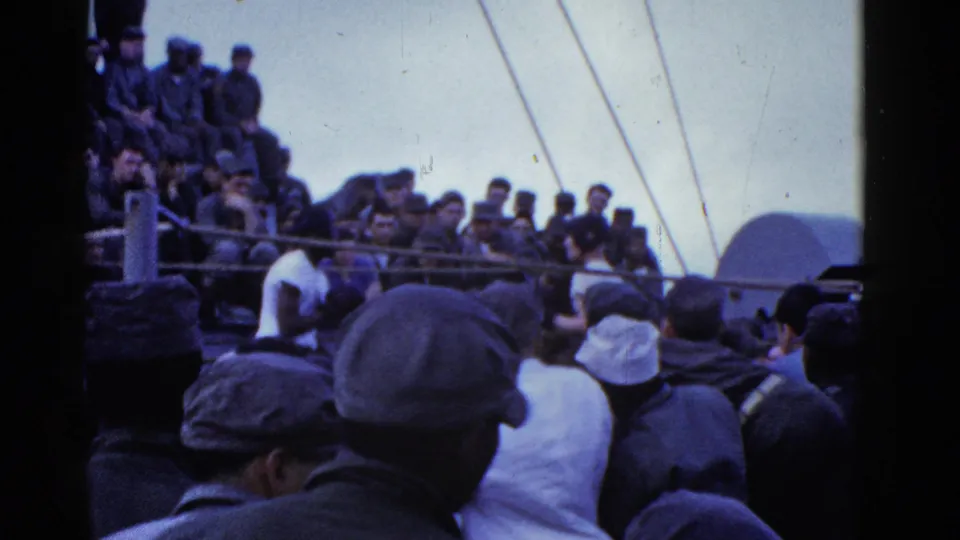 1950s home-movie frame showing a crowded San Francisco ship deck with men in caps, railings, rigging, and foreground onlookers.