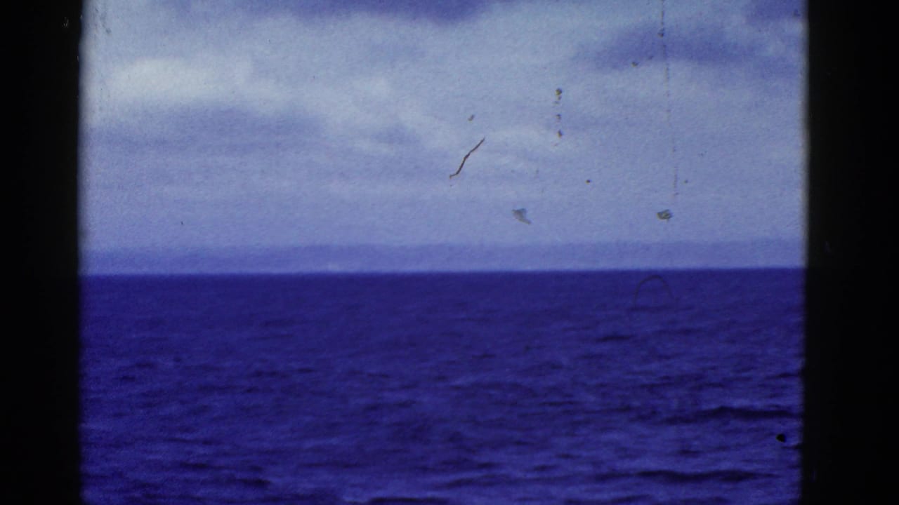 1952 San Francisco-area 8mm frame showing blue water, a low horizon, cloudy sky, and dark vertical edges from a vessel or frame obstruction.