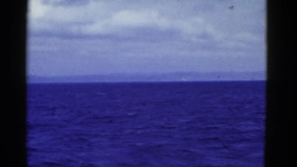 1952 8mm frame from the San Francisco area showing blue water, a faint shoreline or haze, pale cloud cover, and dark borders.