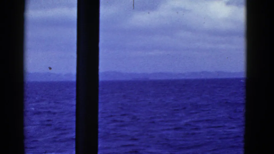 1952 San Francisco home-movie frame showing blue ocean, distant land, and cloudy sky through dark ship-window mullions.