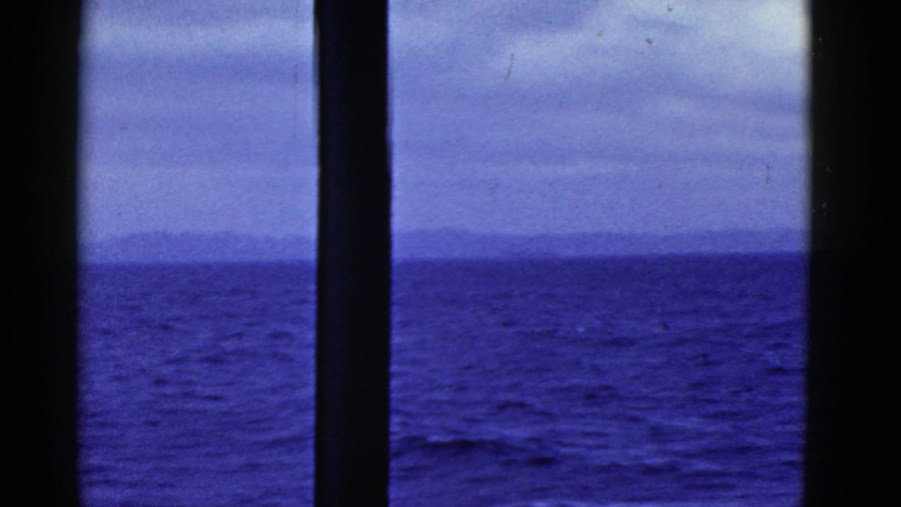 Ocean horizon under clouds, framed by dark ship-window bars.