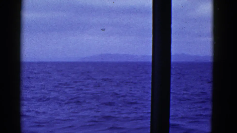 The final frame shows open water, a distant horizon, and ship-window mullions, with blue-shifted 8mm home-movie texture.