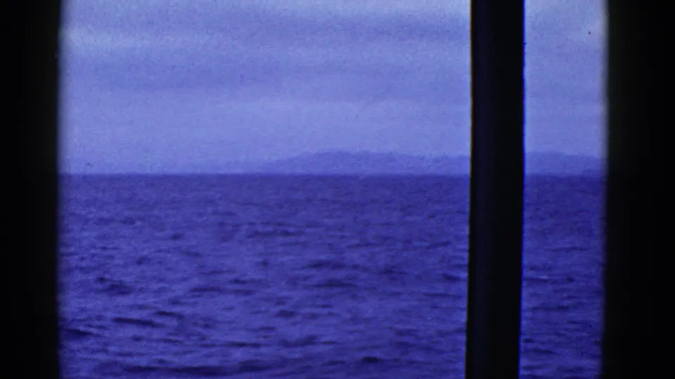 1950s 8mm home-movie view near San Francisco showing choppy bay water, an overcast sky, and distant land through a boat window.