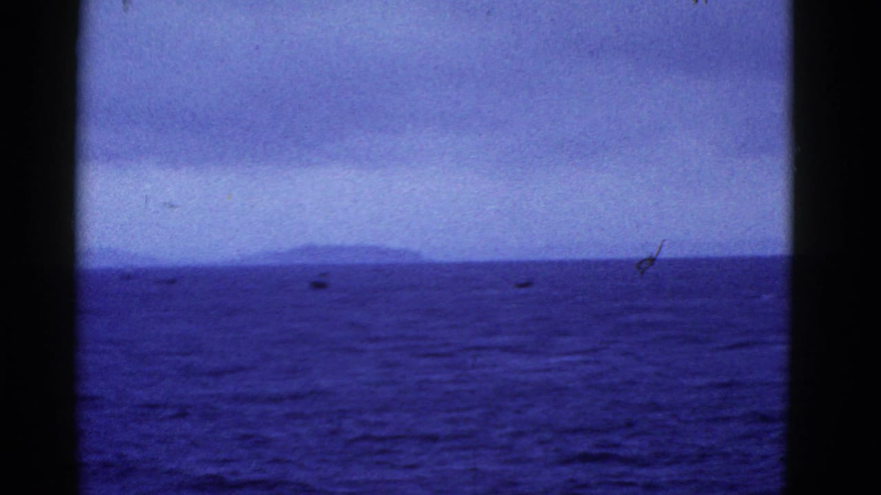 Open water, low distant land, and small dark boats beyond a boat window frame.