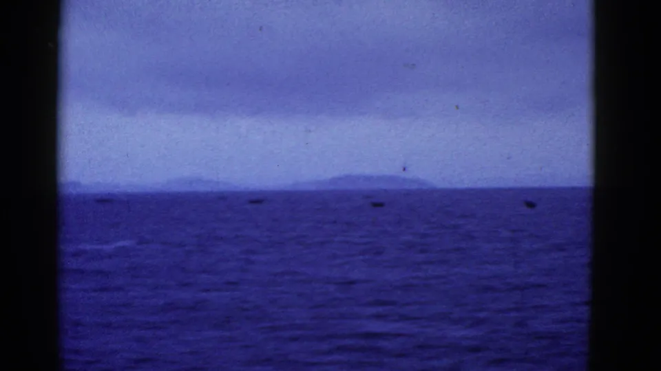 A soft 1950s home-movie seascape near San Francisco shows dark water, cloudy sky, and faint boats or shoreline details at the horizon.
