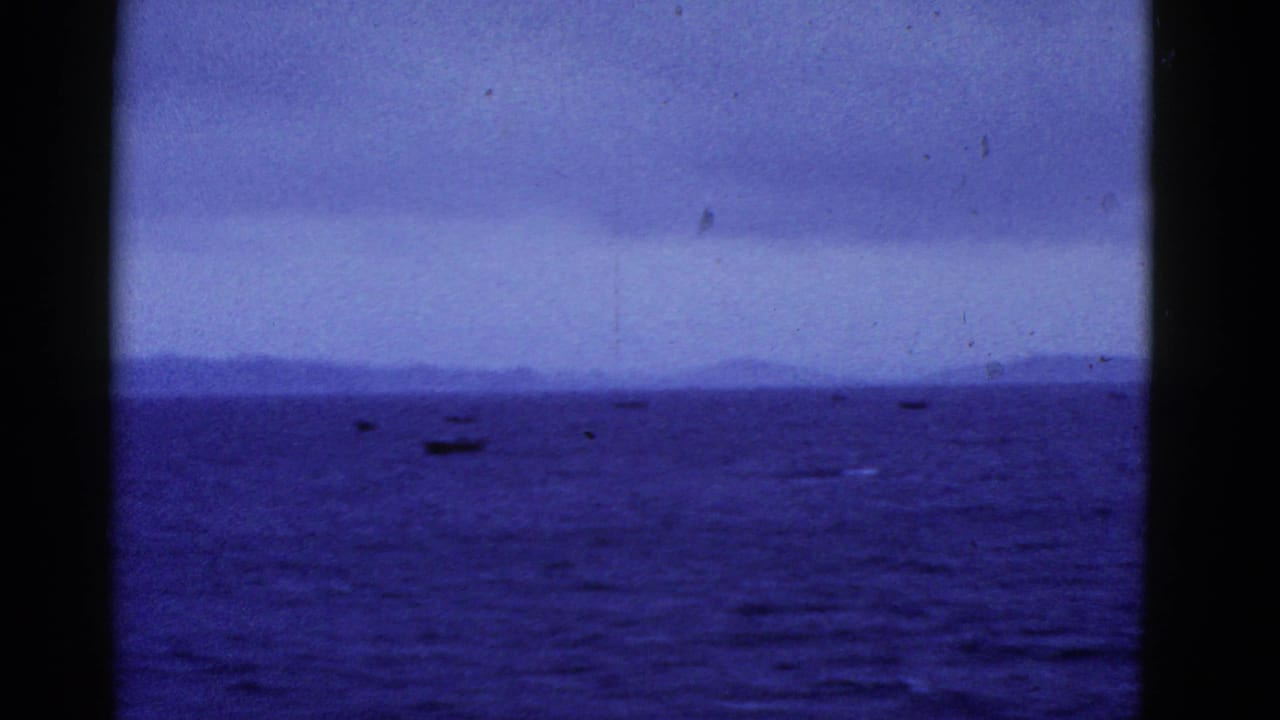 Blue-tinted 8mm frame of small boats on open water near San Francisco, with distant landforms under an overcast sky.