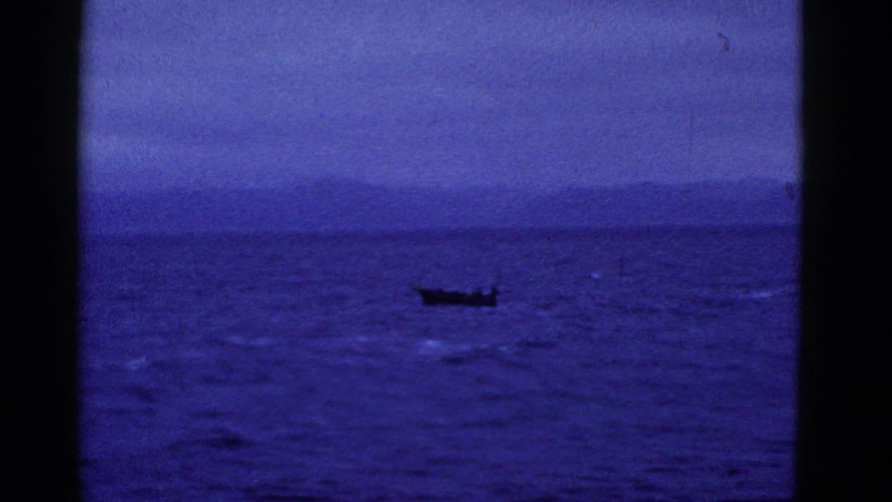 A dark boat crosses choppy water with distant hills along the horizon.