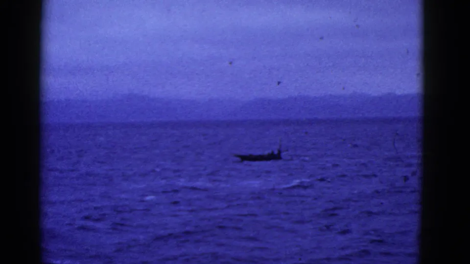 1950s 8mm home-movie frame showing a small dark boat on open water near a distant San Francisco shoreline.