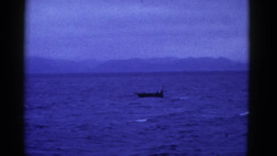 Blue-cast 8mm frame of a small boat on open water, with muted hills and overcast sky near San Francisco.