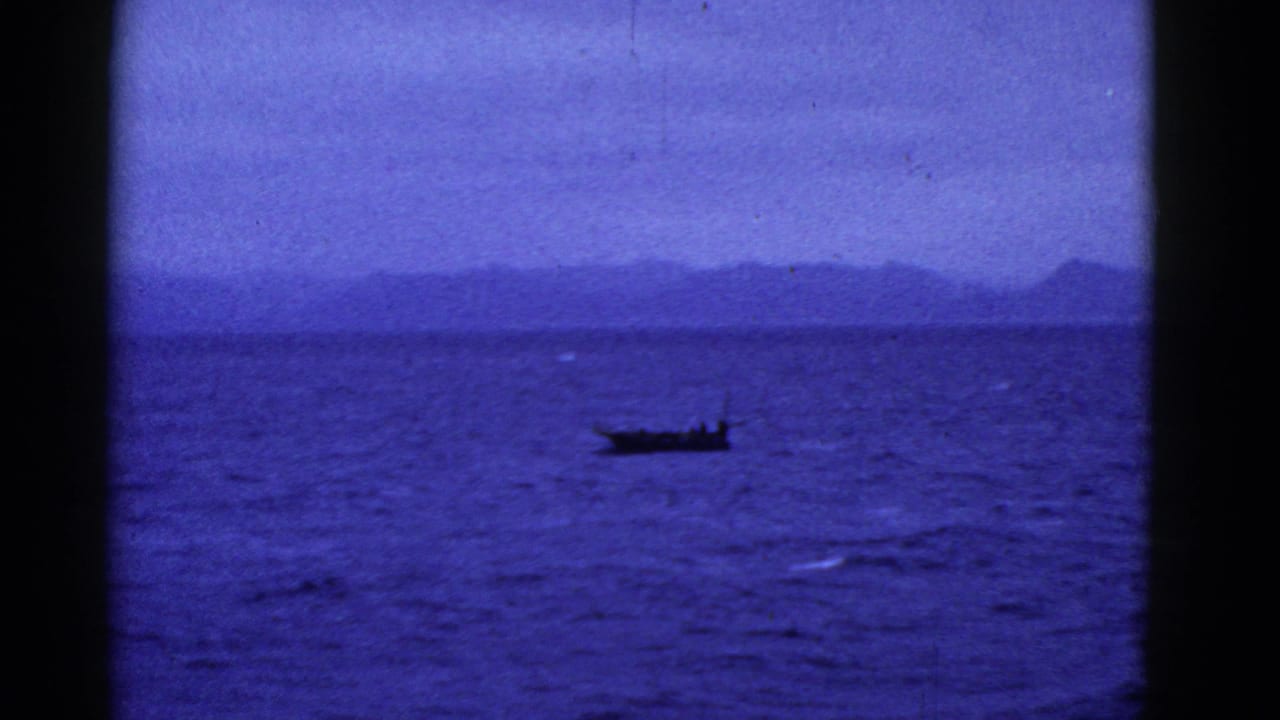 1952 San Francisco-area 8mm frame showing a small dark boat on deep blue water before a hazy distant ridge.