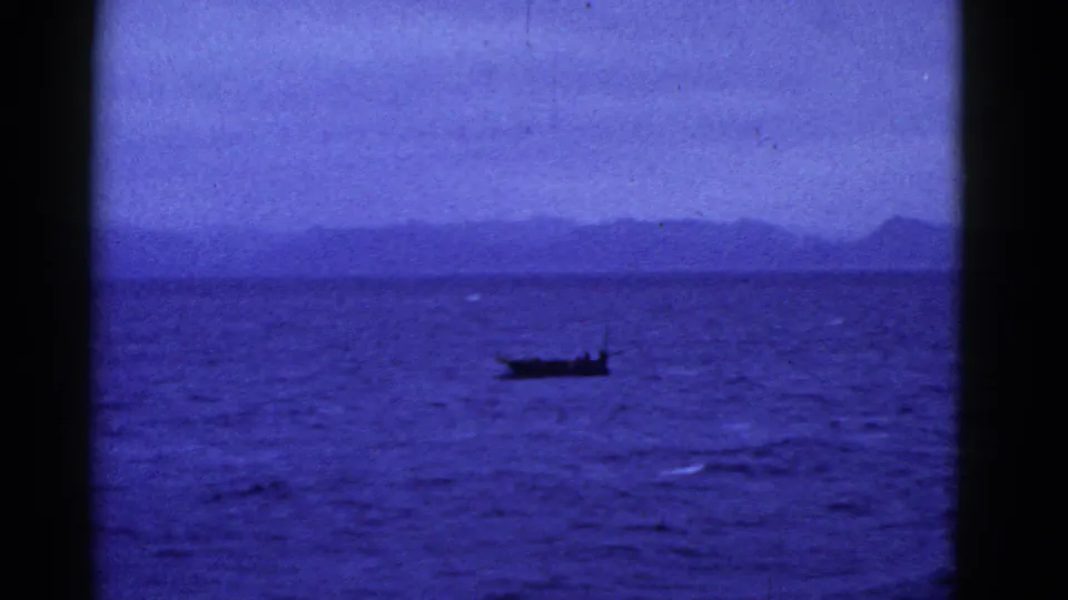 1952 San Francisco-area 8mm frame showing a small dark boat on deep blue water before a hazy distant ridge.