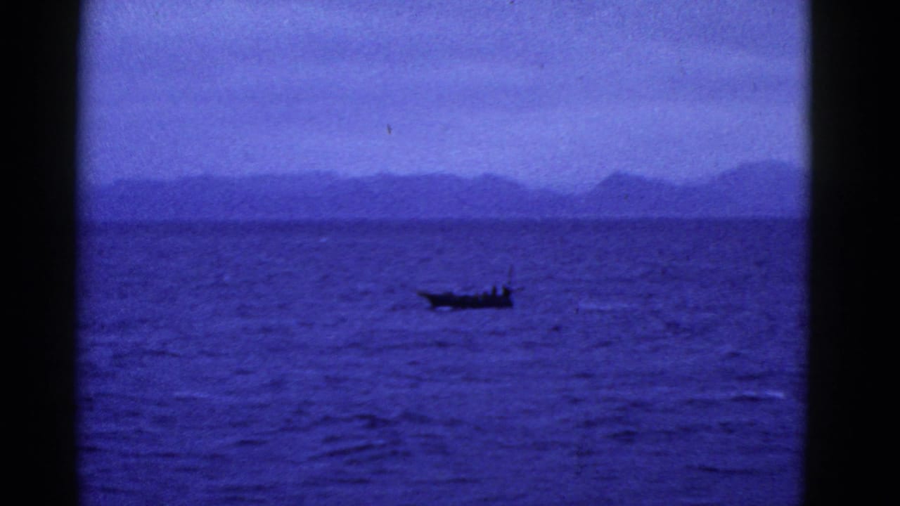 Small boat crossing blue water with distant hills on the horizon.