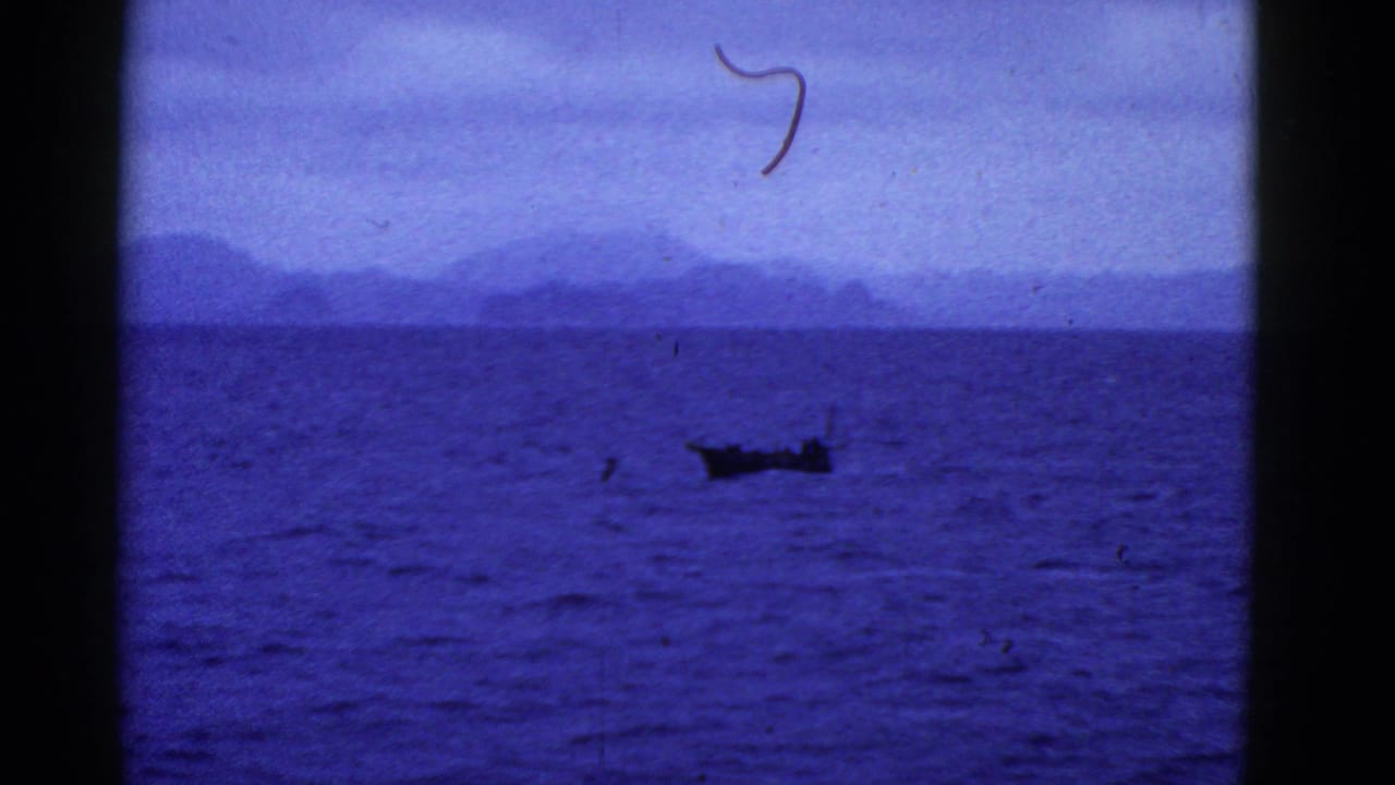 Small boat farther right on dark blue water below a hazy mountain horizon.