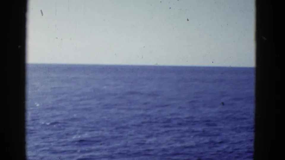 The final 1950s 8mm frame shows mostly open water and pale sky, with grain, dust, and a clean horizon line.