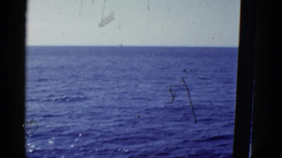 1950s 8mm sea-horizon view near San Francisco, with calm blue water, pale sky, dark frame edges, and visible film scratches.