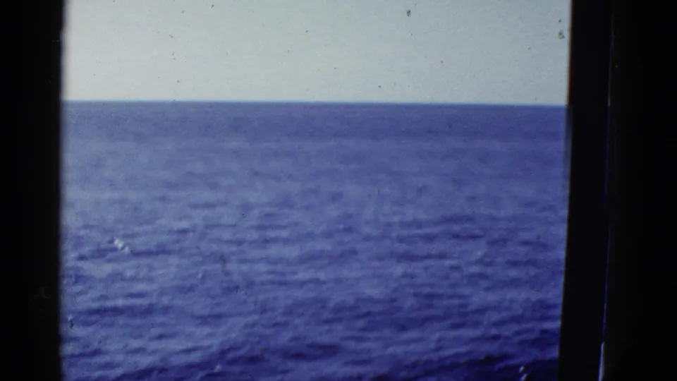 Blue ocean stretches to a pale horizon in this 8mm coastal travel frame, with dark vessel structure at the sides.