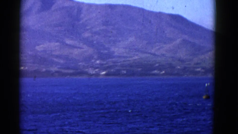 A mountainous shoreline sits across blue water in the final 8mm frame, with a small buoy-like object near the right edge.