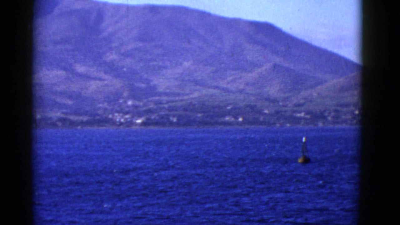 1952 8mm view from a boat on San Francisco Bay, with blue water, a buoy, and a rugged island or shoreline in the distance.