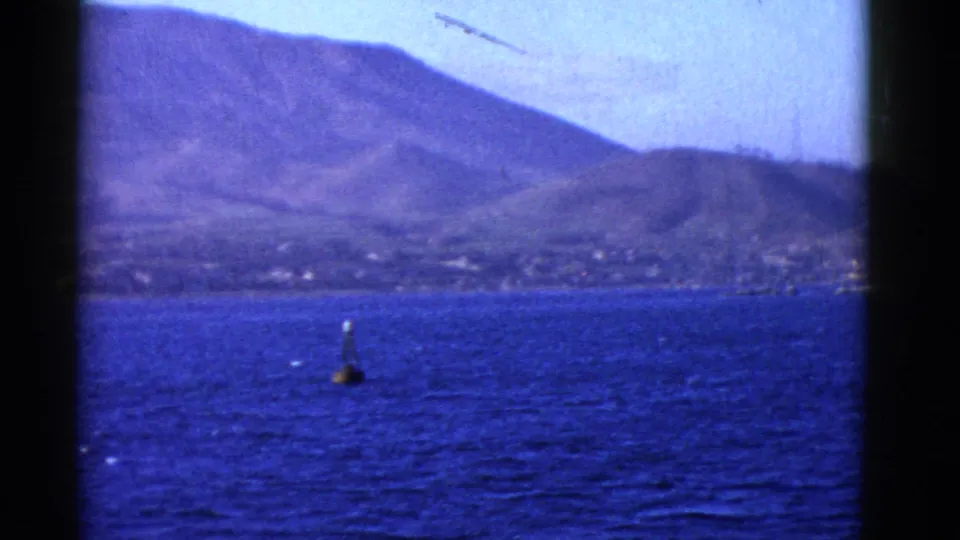 Boat-passenger view of San Francisco Bay in 1952, showing a buoy, sloping coastal hills, and faint buildings along the shore.