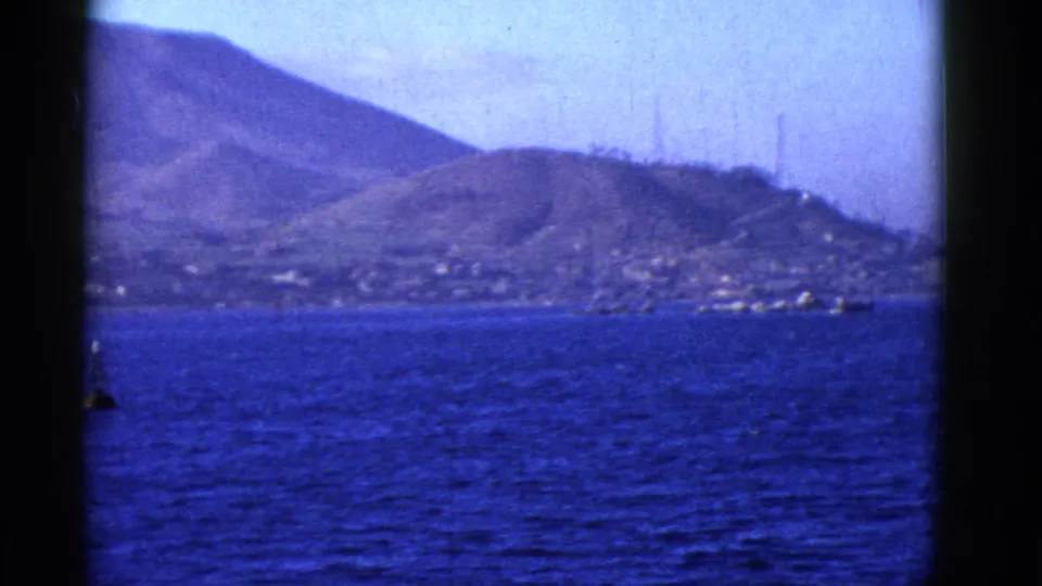 1952 San Francisco Bay footage looking from a boat toward rugged shoreline hills and small distant buildings across blue water.