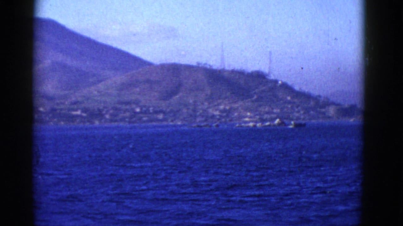 1952 San Francisco Bay area home-movie frame showing blue water, coastal hills, shoreline structures, and soft film grain.