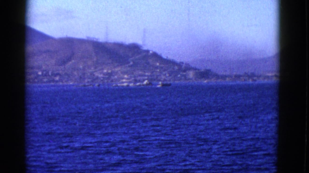 Distant hillside shoreline and small boats seen across blue water through an 8mm frame.