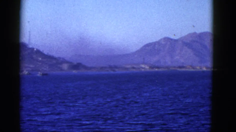 Water-level San Francisco Bay area view with distant hills, low shoreline, blue cast, and visible 8mm frame edges.