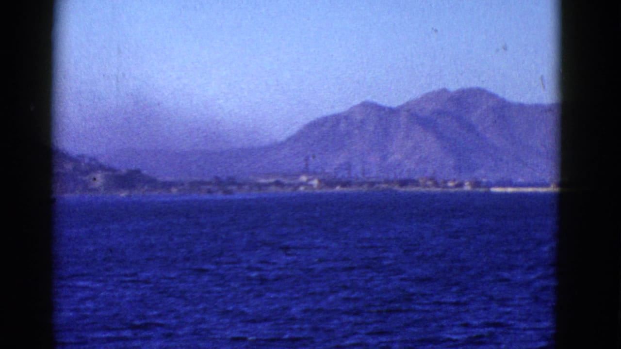 1950s 8mm view across blue water toward a hazy mountainous shoreline near San Francisco, framed by dark film edges.
